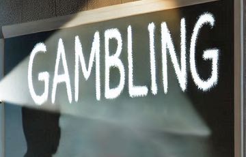 En svart tavla med ordet 'GAMBLING' skrivet med stora vita bokstäver, belyst av en strålkastare.